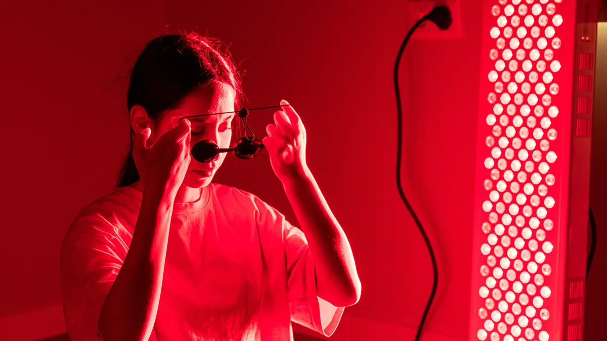 A woman putting on goggles in front of a red light panel